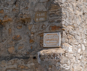 Greek street and entry signs mounted on a weathered stone wall in Mesta village at Chios island, Greece