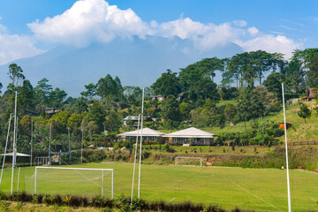 Green soccer field sits nestled within the cool highlands of Puncak, Bogor, surrounded by lush pine trees and a majestic mountain backdrop under a clear blue sky. © Fani