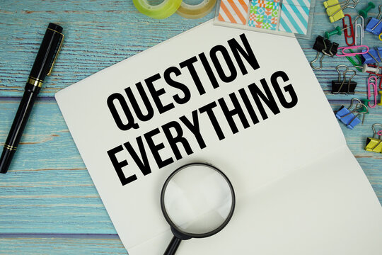 Question Everything text on a paper surrounded by office supplies and magnifying glass on a blue wooden surface