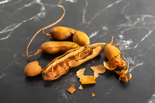 Broken tamarind pods with pulp and shell pieces, tropical fruit ingredient, Indian cuisine, tangy flavor, marble background, closeup food photography
