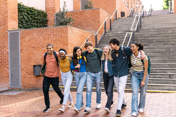 Group of diverse college students laughing and walking arm in arm on an outdoor university campus. Friendship and education