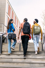 Obraz premium Diverse group of young students walking down university stairs, carrying backpacks and books while engaging in conversation
