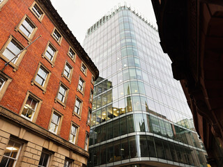 Fototapeta premium Modern glass tower beside red brick building in Manchester city center, striking urban architecture scene