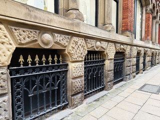 Naklejka premium Historic stone building with ornate iron railings along a Manchester street in the UK