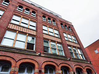 Naklejka premium Brick building in Manchester, UK with arched windows and decorative facade in an urban street scene