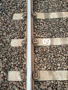 Top view of a steel railway track on concrete sleepers and grey ballast stones. Detailed texture of industrial transportation infrastructure and logistics background.