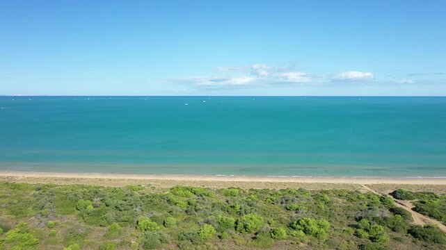 Wide aerial shot of the pristine sandy beach and lush greenery at Isola Varano Nature Reserve, Italy, with calm turquoise sea under a clear blue sky.