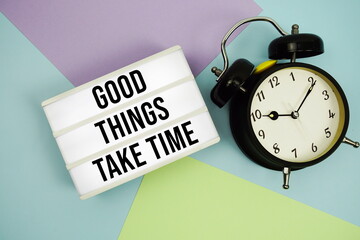 Good Things Take Time text in lightbox with alarm clock flat lay on multicolor pastel background