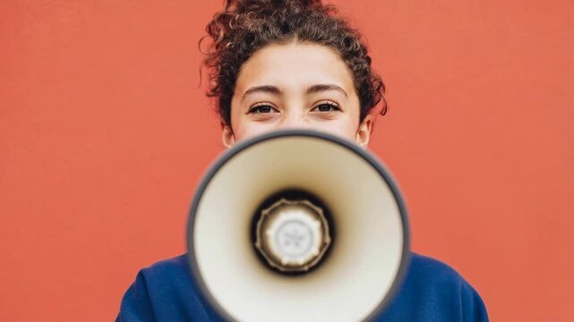 Young woman enthusiastically speaking through megaphone against bold colorful background expressing empowerment confidence and public communication energy