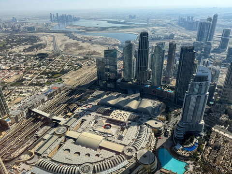 Aerial high angle view of Downtown Dubai skyscrapers and modern urban infrastructure from the Burj Khalifa observation deck with the Persian Gulf in the background.
