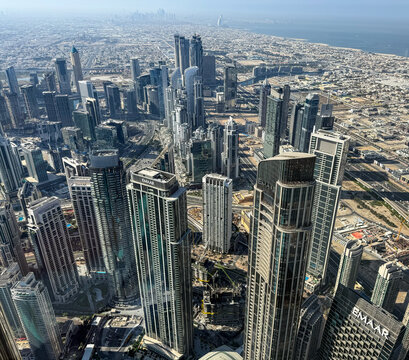 Aerial high angle view of Downtown Dubai skyscrapers and modern urban infrastructure from the Burj Khalifa observation deck with the Persian Gulf in the background.
