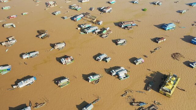 Aerial view of the floating village of Chong Kneas on Tonle Sap Lake, Cambodia, featuring scattered houseboats and muddy water. Unique rural lifestyle and traditional architecture are visible from