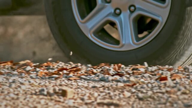 Close up view of car wheel driving on gravel road during sunny day creating dust clouds in rural landscape setting showing off road transportation performance