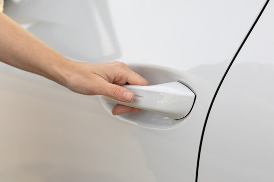 Hand reaching for white car door handle, showcasing modern vehicle design and sleek exterior, emphasizing accessibility and user-friendly features in automotive context
