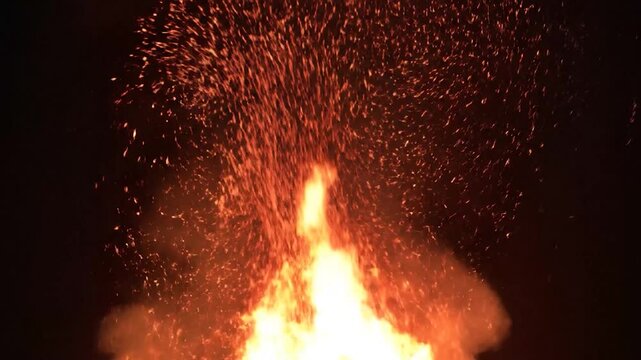 Vibrant bonfire flames and glowing embers illuminate the dark night sky