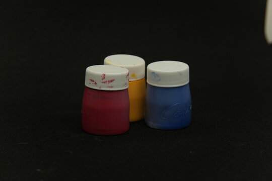 Three small paint jars in primary colors red yellow and blue on dark background with copy space