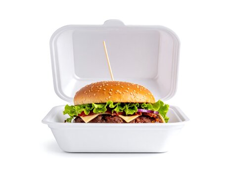Burger with fixings in styrofoam takeout container, bright lighting