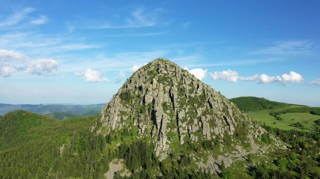 Aerial view of the rugged Mont de Gerbier de Jonc, a distinctive volcanic mountain surrounded by lush green forests and rolling hills in the Ardeche region of France.