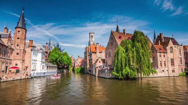 Canal in historic city of bruges with ancient brick buildings and green trees under blue sky reflecting on water during sunny summer day in belgium town