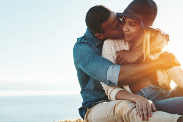 Obraz premium Happy couple, relax and hug at beach with kiss on vacation with bonding, love and space in sunshine. Man, woman and smile with interracial relationship, embrace and affection on seaside holiday