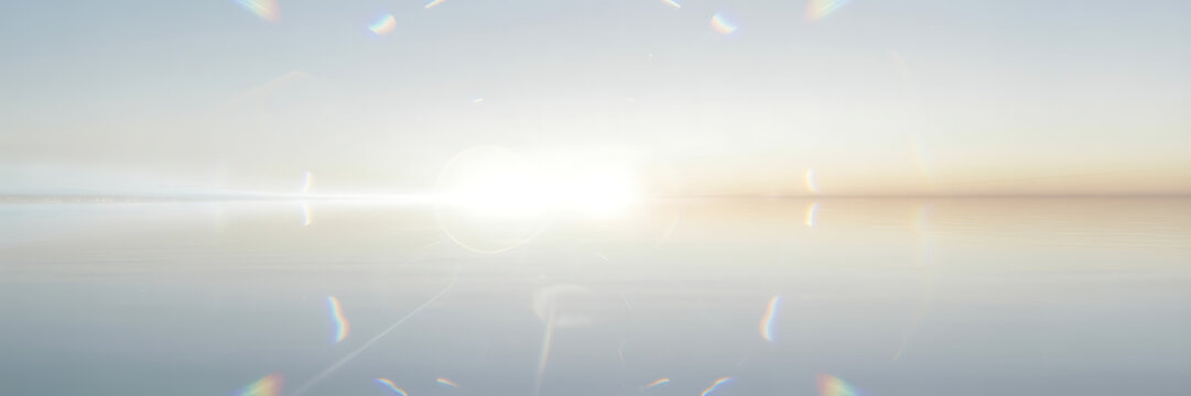 Bright, abstract sun glare with rainbow lens flares reflecting over a calm, light blue water surface