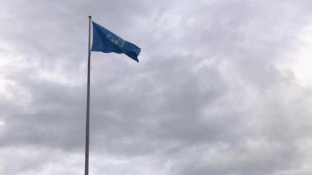 The United Nations flag waves proudly in the wind against a backdrop of cloudy skies, symbolizing global unity and cooperation.