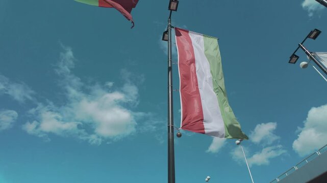 The Italian flag waves proudly in the wind against a bright blue sky with fluffy white clouds, evoking feelings of patriotism and national pride.