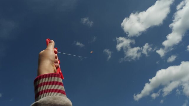 A child s hand holds a kite string, while a kite dances in the sky, symbolizing