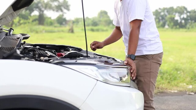 unrecognized man is opening the hood of a car outdoors, checking or fixing the car engine on the road after a car breakdown