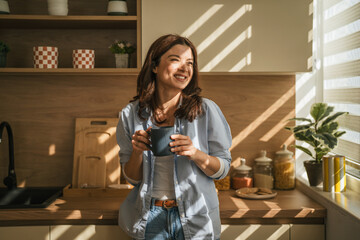 Woman enjoying morning coffee in sunlit modern kitchen