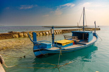Obraz premium Blue fishing boat rests calm by stone breakwater