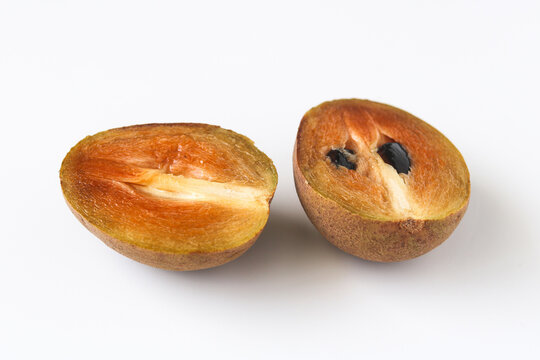 A single sapodilla (sawo manila) fruit sliced in half, revealing its rich, caramel-colored flesh.