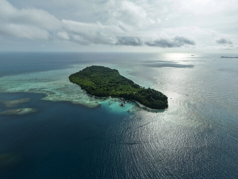 Aerial view of a verdant island embraced by turquoise shallows and deep blue waters, Menjangan Kecil Island, Karimunjawa, Central Java, Indonesia.