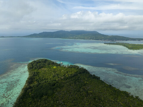 Aerial view of lush green vegetation meets the turquoise waters, a contrast of textures under a cloudy sky, Menjangan Kecil Island, Karimunjawa, Central Java, Indonesia.