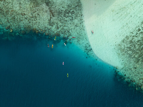 Aerial view of turquoise waters meet the sandy shore, kayaks dotting the deep blue, a tranquil contrast of colors and textures at Menjangan Kecil Island, Karimunjawa, Indonesia.