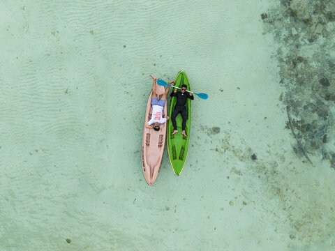 Aerial view of two people relaxing on kayaks in the crystal-clear turquoise waters surrounding Menjangan Kecil Island, Karimunjawa, Central Java, Indonesia.
