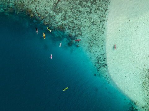 Aerial view of kayaks and paddleboards scattered across the turquoise waters near Menjangan Kecil Island, contrasting with the white sandy beach, Karimunjawa, Central Java, Indonesia.