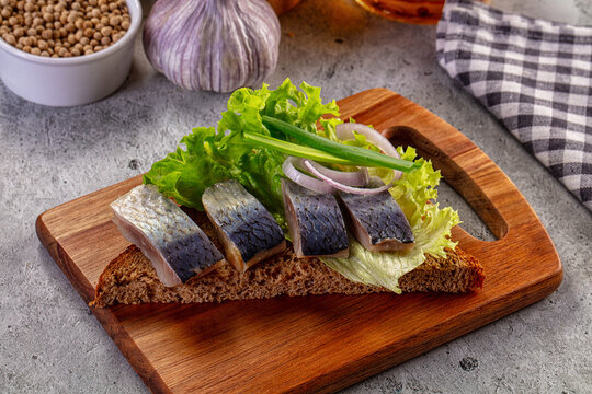 Salted herring appetizer on dark rye bread with lettuce and onions on a wooden board