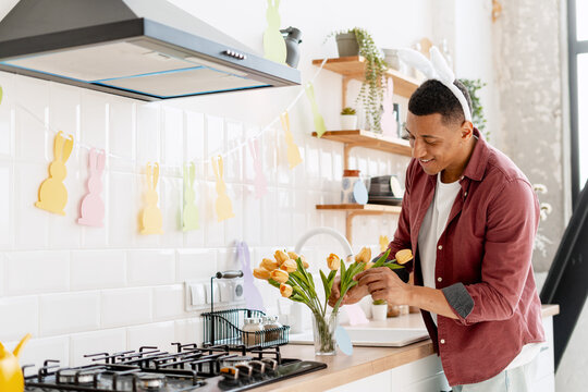 Smiling man wearing bunny ears arranging tulips celebrating happy Easter at home