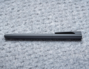 A black pen lies on a grey textured surface, viewed from directly above.