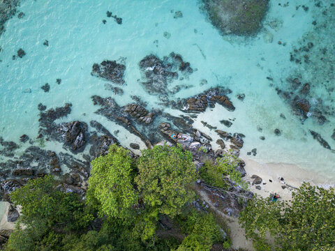 Aerial view of turquoise waters meet rugged rocks and verdant trees at Tanjung Gelam Beach, a tropical oasis, Karimunjawa, Central Java, Indonesia.