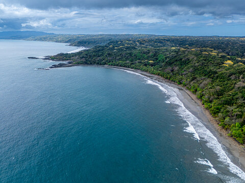 Aerial view of the dark blue sea meeting the sandy shore at the edge of a lush green forest, Tango Mar, Puntarenas Province, Costa Rica.