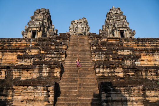 Woman descending steep stone stairs of ta keo temple with clear blue sky
