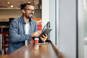 Man smiling typing on digital tablet with wireless earbuds