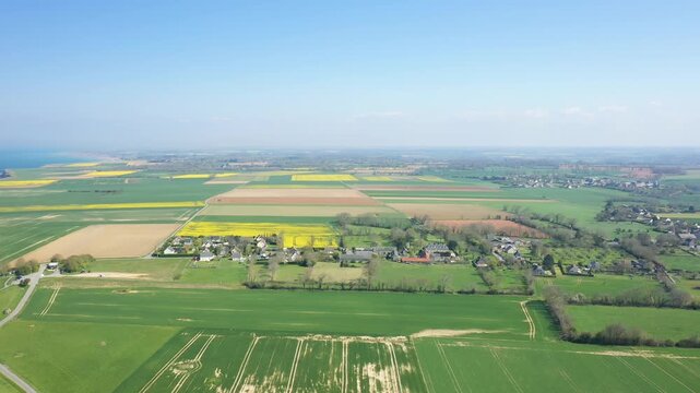 Drone shot of green and yellow patchwork fields and rural village houses in the Longues sur Mer region of Normandy, France, under a clear blue sky.