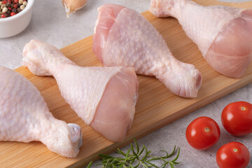 Fresh chicken drumsticks and vegetables on a cutting board in a kitchen setting ready for cooking