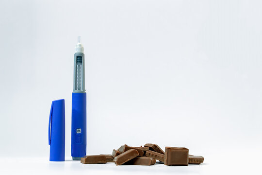 Blue insulin injector pen like ozempic standing next to milk chocolate pieces isolated on a white background, diabetes medication and glucose management concept, glp-1, semaglutide, copy space