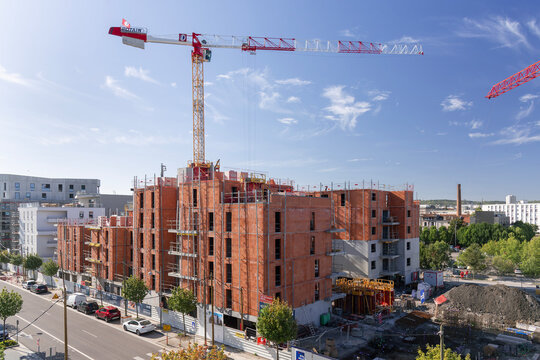 Nancy, France - September 19th 2019 : View on a flat-top tower crane Potain MDT 219 crane with a building under construction with its orange brick facades and formwork at the top.