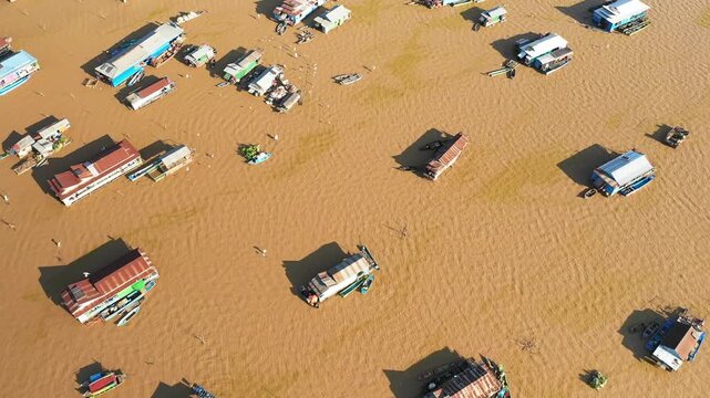 Aerial view of floating houses and boats scattered across muddy water in the Chong Kneas floating village, Cambodia. Unique rural lifestyle and architecture on the water.