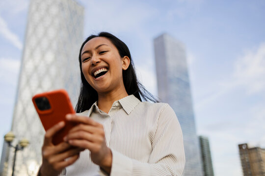 Laughing business professional using smartphone outdoors in city